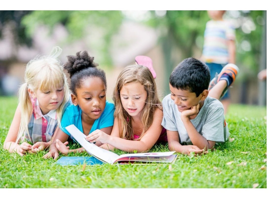 four kids reading a book in the grass